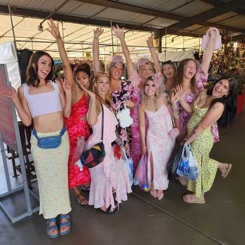 A group of women pose and wave together indoors under a canopy.