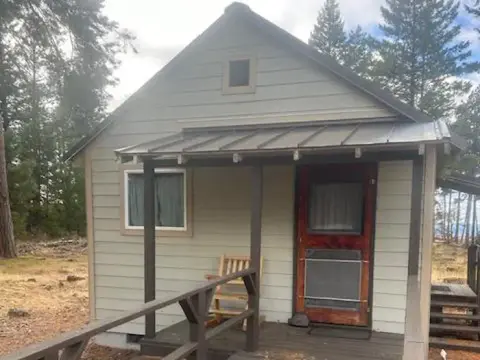 A small cabin with a covered porch stands among trees.