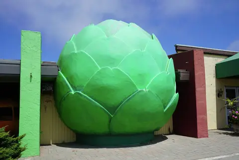 A giant green artichoke sculpture sits outside a building.
