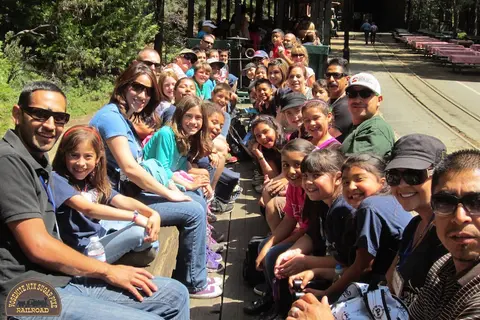A group of people smiling together while riding on an open-air train.
