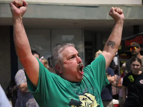 A man raises his arms in celebration outdoors amidst a crowd.