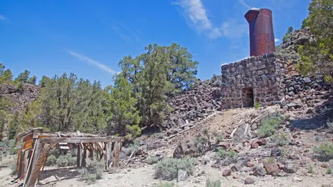 An old stone and metal structure sits on a rocky hillside among trees.