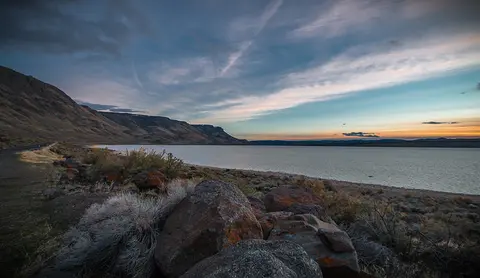 A scenic landscape view of a lake with hills and a sunset sky.