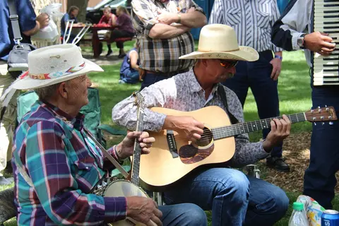 Two men playing music outdoors together with stringed instruments.