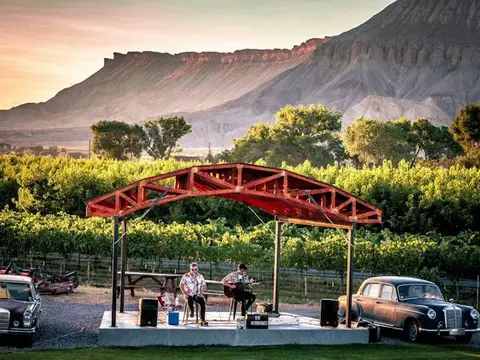 Two musicians perform on an outdoor stage in front of a mountain landscape.