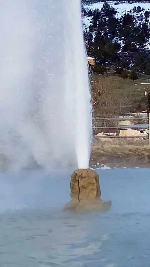 A geyser erupts from a rocky formation in a pool of water.