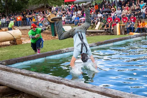 A competitor falls backwards into a pool as a clown watches during an outdoor event.