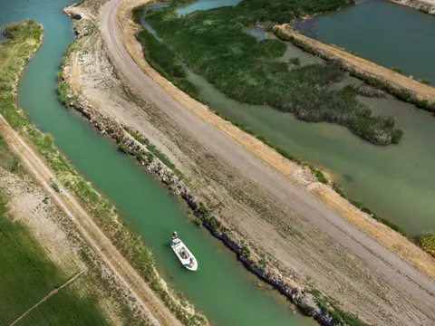 An aerial view shows a boat navigating a narrow waterway between grassy banks.