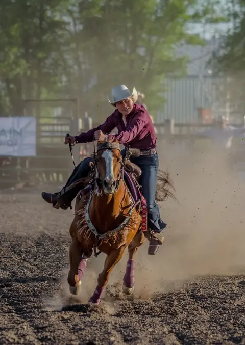 A person rides a horse at high speed in a dusty arena.
