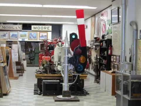 An indoor museum displaying historical artifacts, a red vehicle, a train signal, and signs.