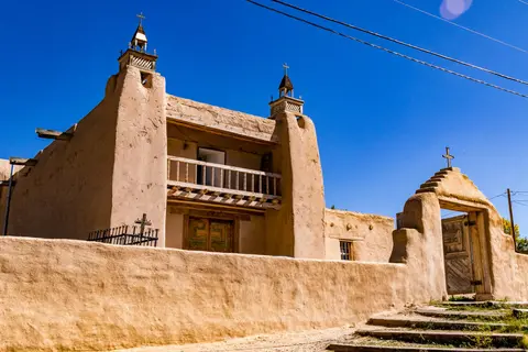 A historic adobe mission church viewed from the front under a clear blue sky.