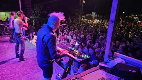 A band performs on an outdoor stage before a large crowd at night.