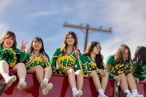 A row of cheerleaders sitting on a float and smiling.