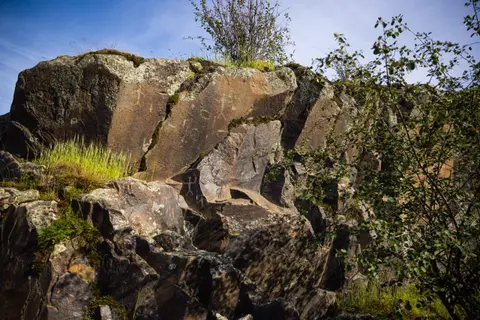 A rock formation with petroglyphs and sparse vegetation against a blue sky.