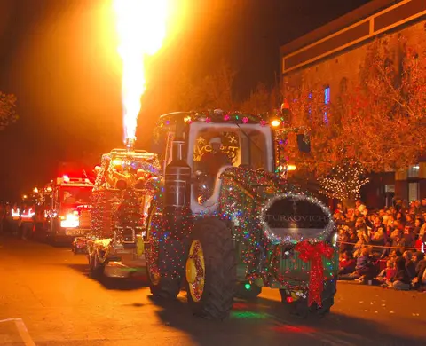 A decorated tractor and fire engine in a nighttime parade with a crowd watching.
