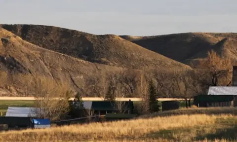 A rural landscape showing buildings nestled below rolling hills.