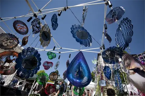 Various metal wind spinners hanging from a canopy structure outdoors.