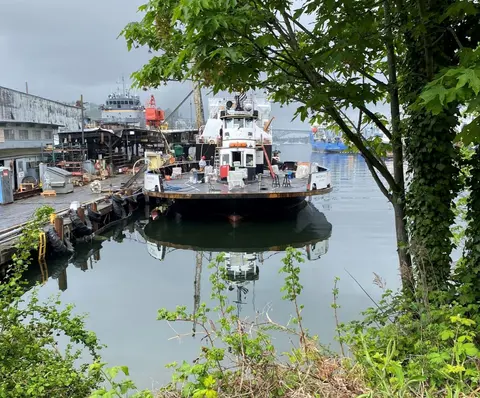 A tugboat is moored at a shipyard dock on calm water.