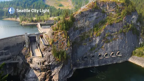 Aerial view of a hydroelectric dam and rocky cliffs with a water reservoir and forest.