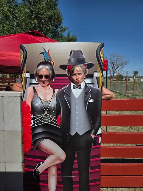 Two people pose behind a cutout photo board depicting a 1920s couple.