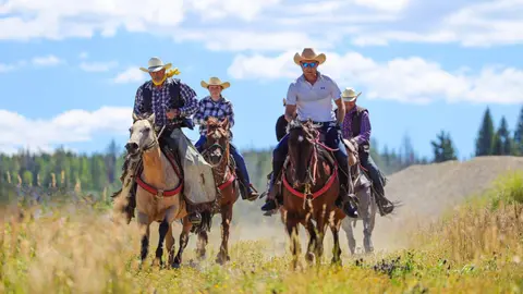 A group of people wearing cowboy hats ride horses across a field.