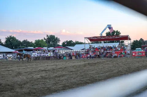 A person rides a horse in a rodeo arena before a seated crowd.