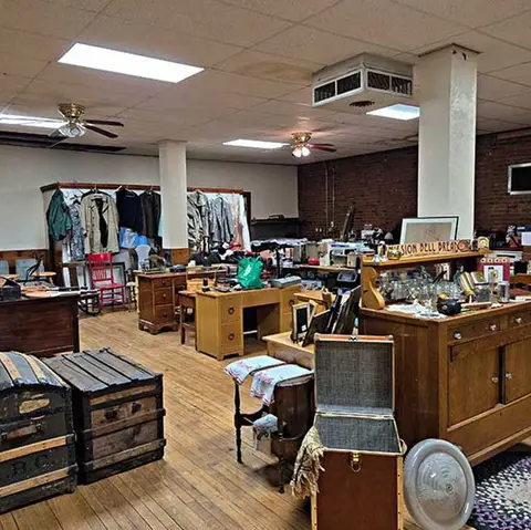 An interior view of an antique or thrift shop filled with vintage furniture, clothing, and household items.