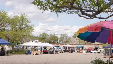 An outdoor market with tents and people browsing under a colorful umbrella.