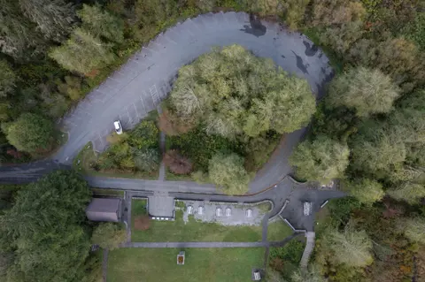 An aerial view of a parking lot and picnic area surrounded by dense trees.