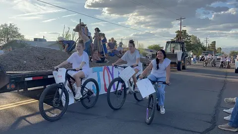 Three young people ride bicycles in a parade on a street.