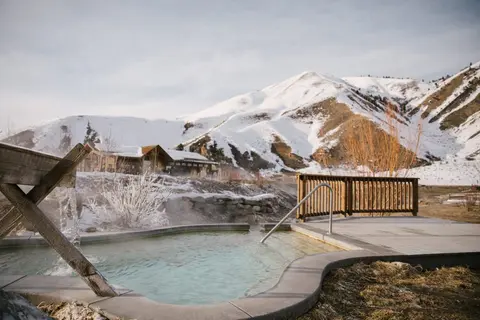 An outdoor hot spring pool with snow-capped mountains in the background.