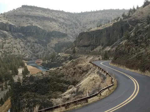 A winding road curves along a hillside next to a river running through a canyon.