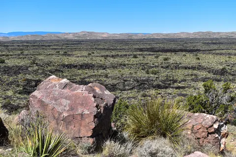 A vast desert landscape featuring dark volcanic rock fields under a clear blue sky.