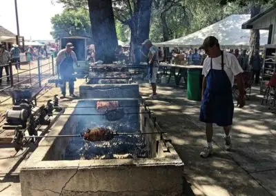 People cooking meat on large outdoor spits.