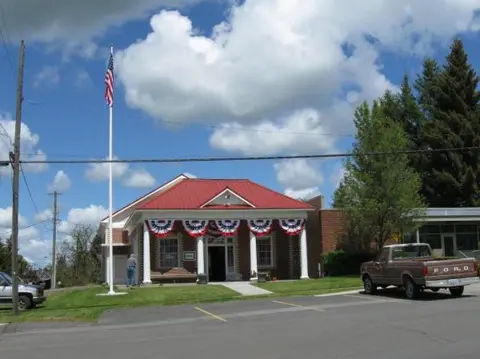An exterior view of a brick building decorated with patriotic bunting and a flagpole.