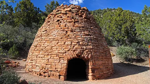 A stone beehive kiln stands in a wooded area.