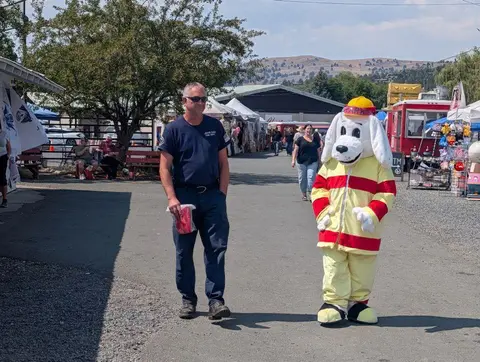 A man in a uniform walks alongside a dog mascot at an outdoor event.