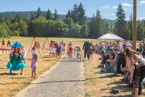 A crowd of people gathers outdoors to watch a race or event on a gravel path.