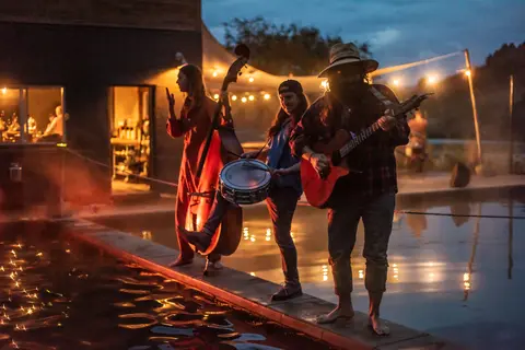 A band plays music near a pool at dusk.