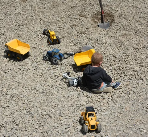 A child plays with toy trucks in a gravel area.