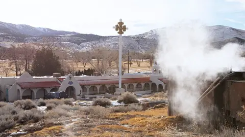 An outdoor view of a mission-style building with steam rising from a structure in the foreground.
