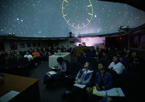 People look up at a star-filled dome inside a planetarium.