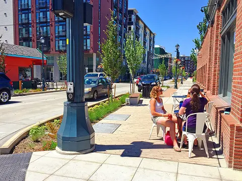 People sit at an outdoor table on a sunny sidewalk.