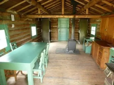 Interior of a rustic wooden cabin with a dining table and stove.