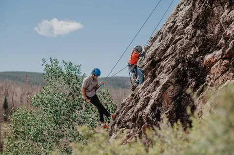 People rock climbing and rappelling on a rocky cliff outdoors.