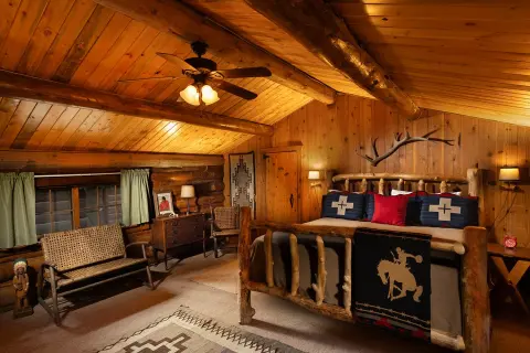 A rustic bedroom with log walls, wooden ceiling beams, and a log-frame bed.
