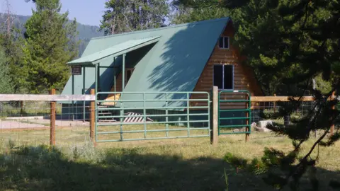 A rustic wooden cabin with a green metal roof stands behind a fenced yard.