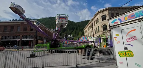 An amusement park ride set up on a street with historic buildings and mountains in the background.