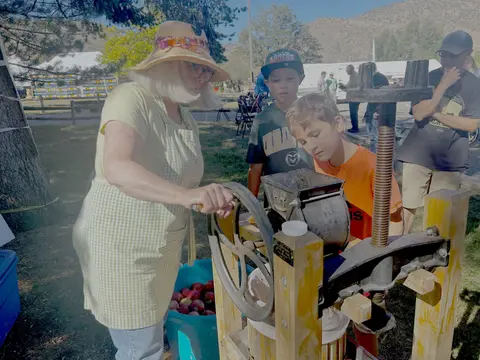 A woman and children operate an apple cider press outdoors.