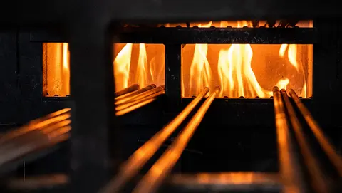 Bright flames burn inside a furnace with metal bars extending outward.